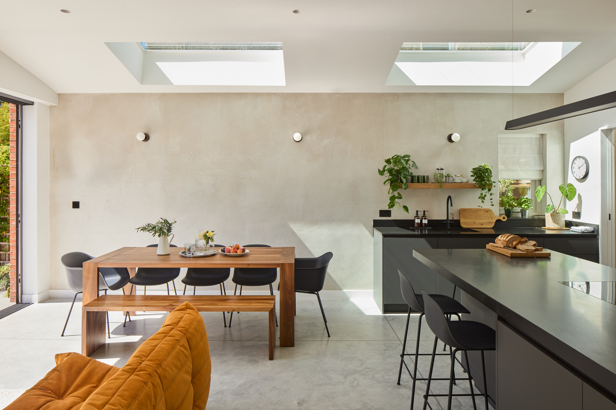 Modern open-plan kitchen with rooflights, timber dining table, and dark matte worktops